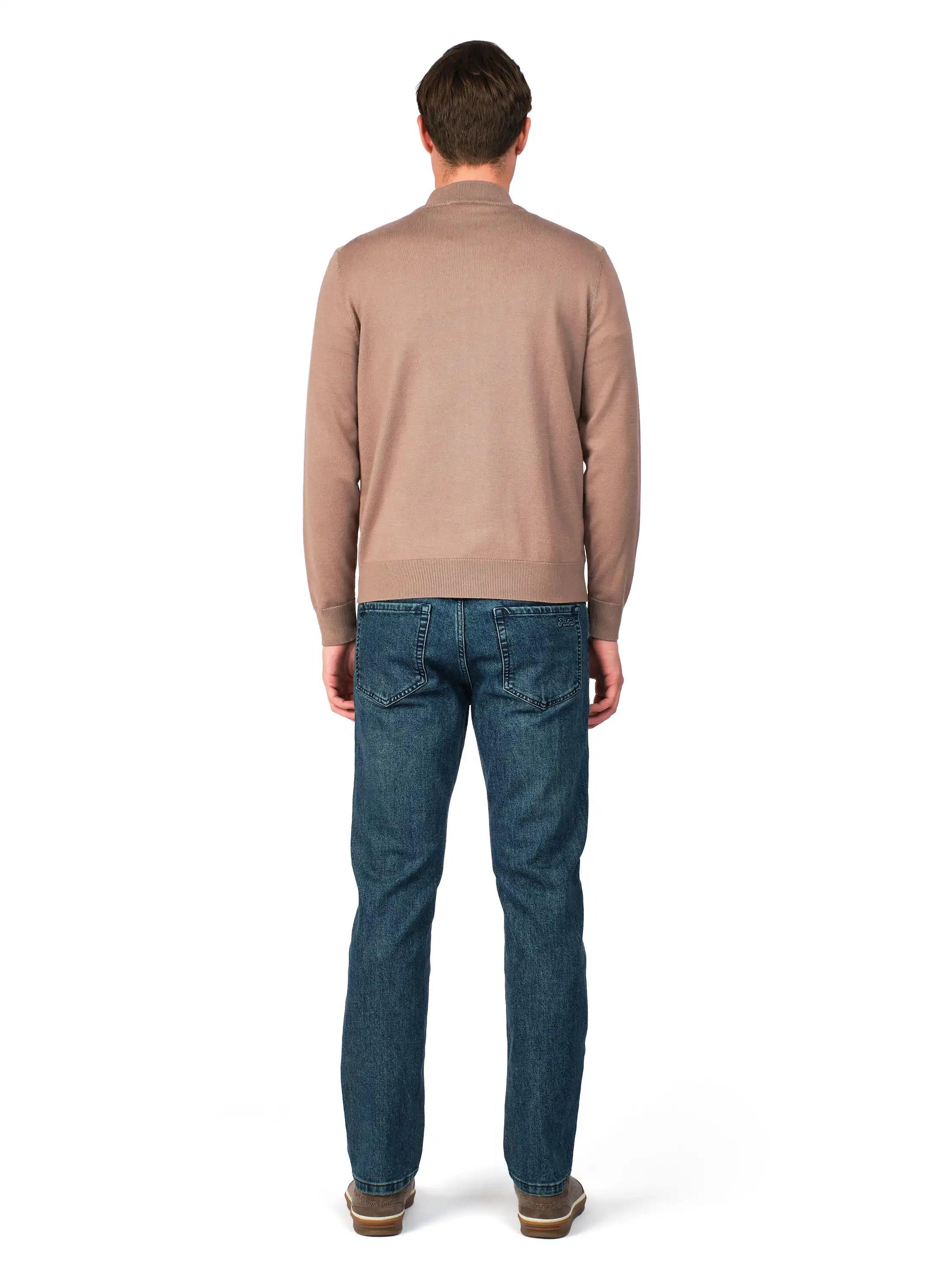 Man wearing a beige sweater and blue jeans on a white background