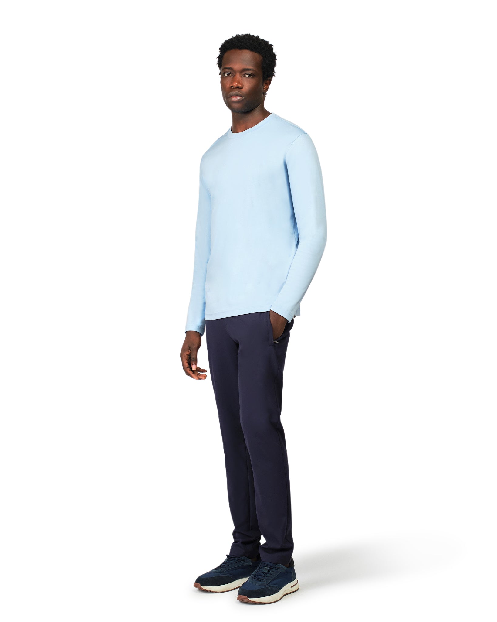 Man wearing a light blue sweater and dark pants on a white background