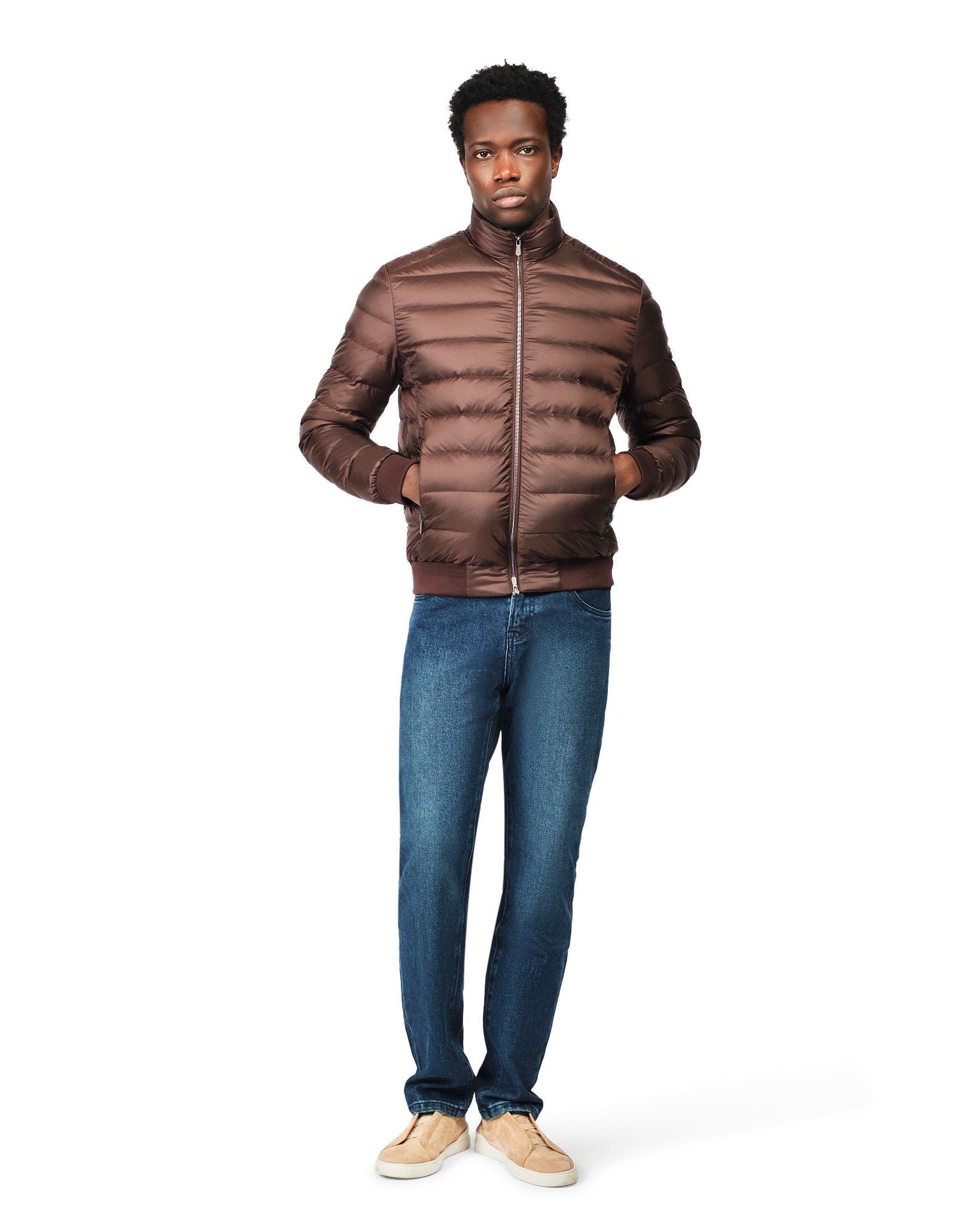 Man wearing a brown puffer jacket and blue jeans on a white background