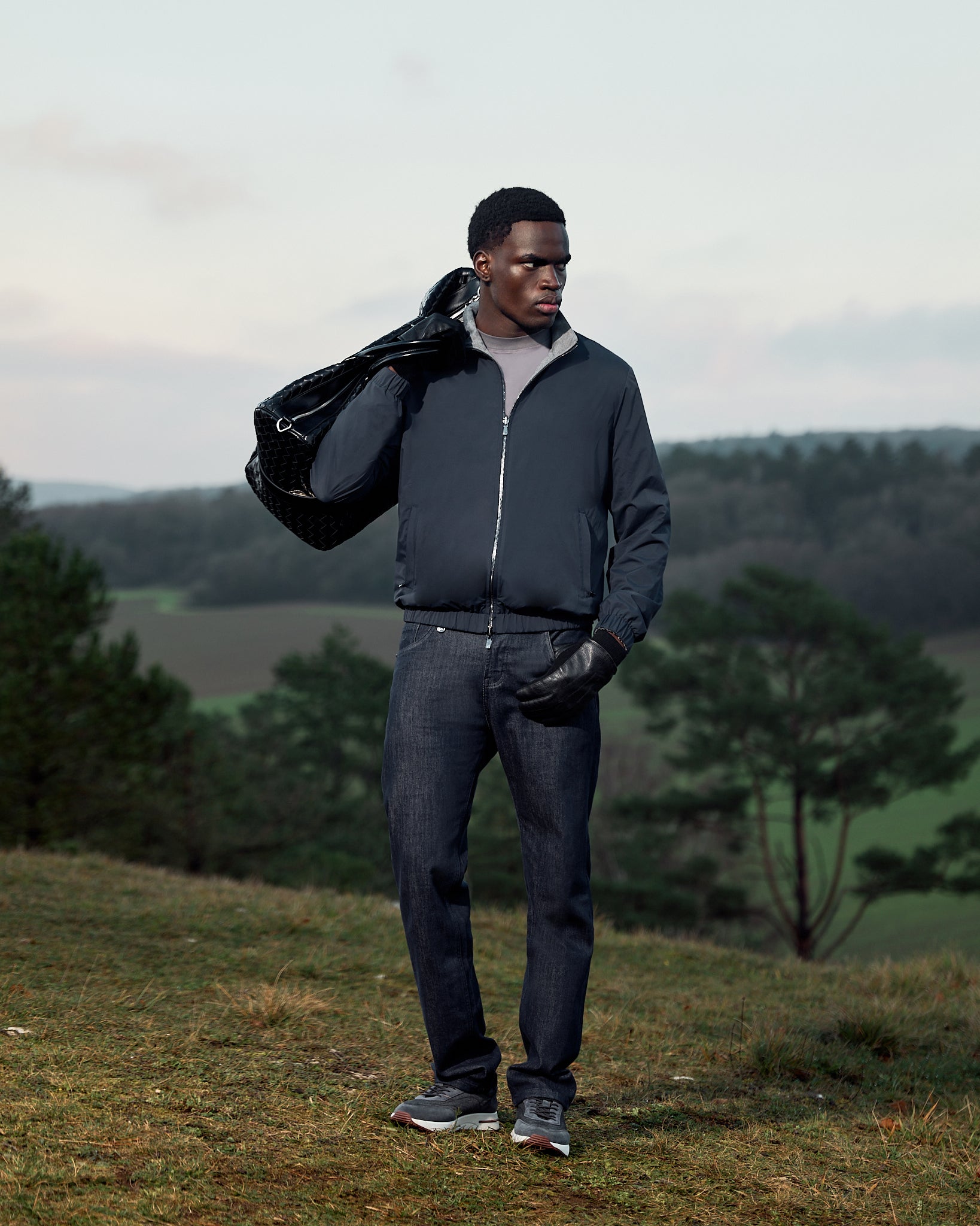 Man holding a black bag outdoors with greenery in the background