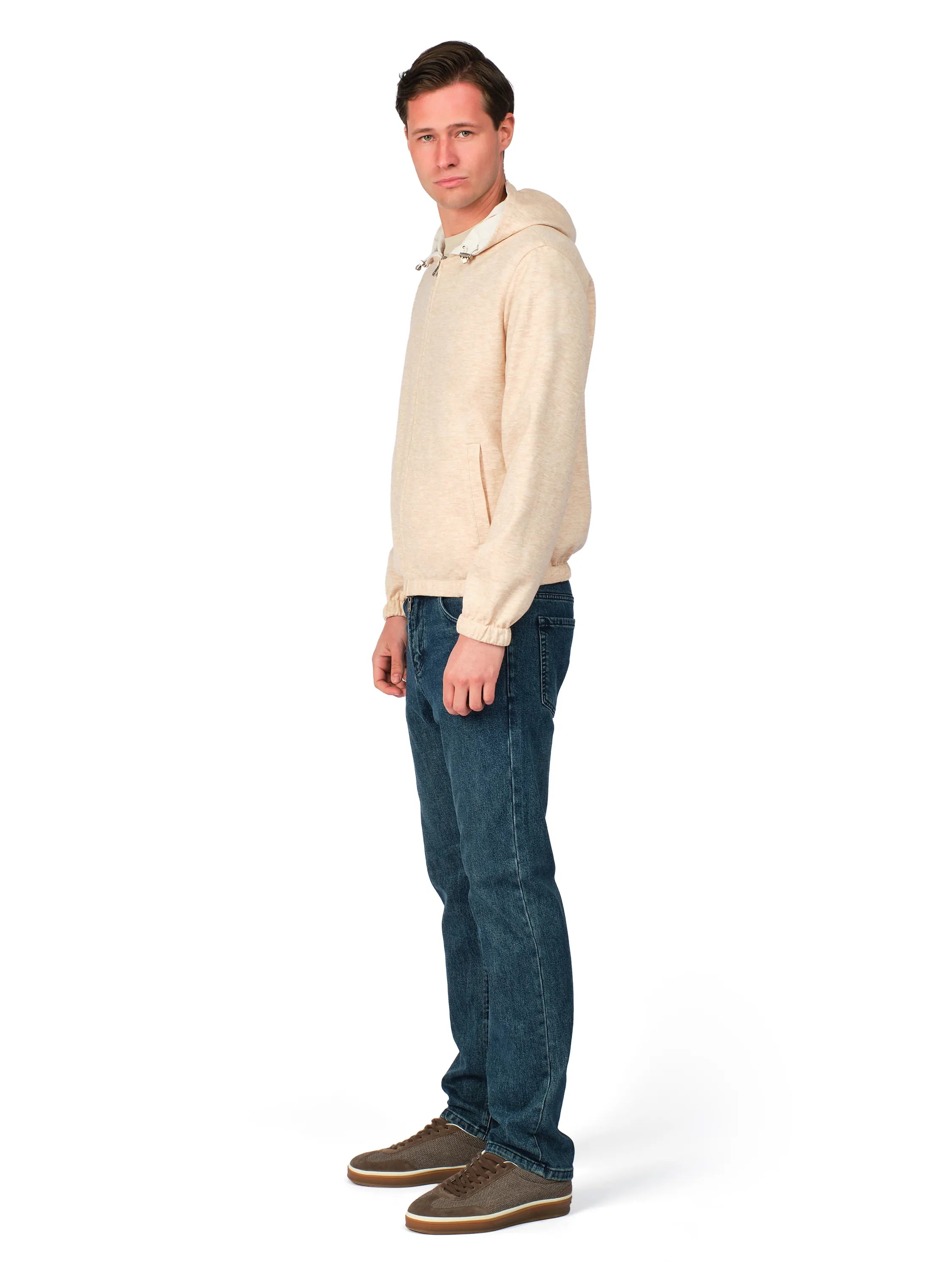 Man wearing a beige hoodie and blue jeans on a white background