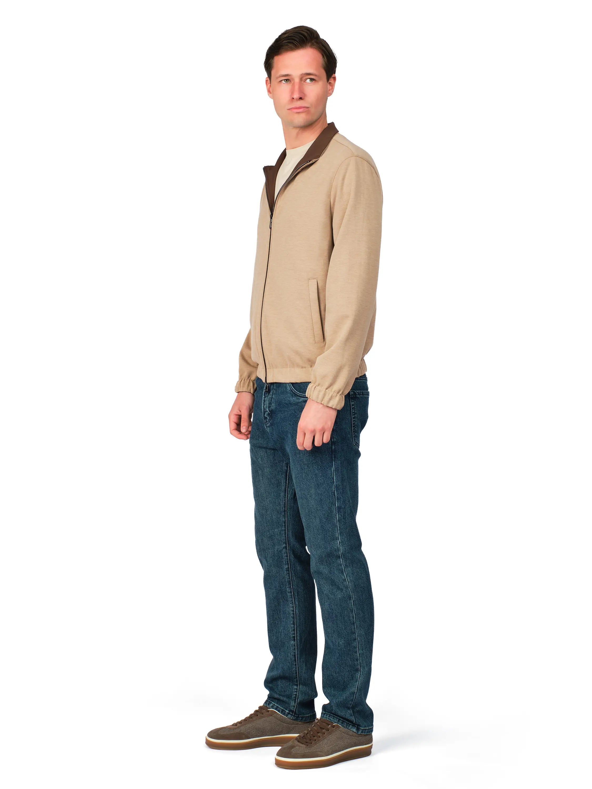 Man wearing a beige sweater with a brown collar and blue jeans on a white background
