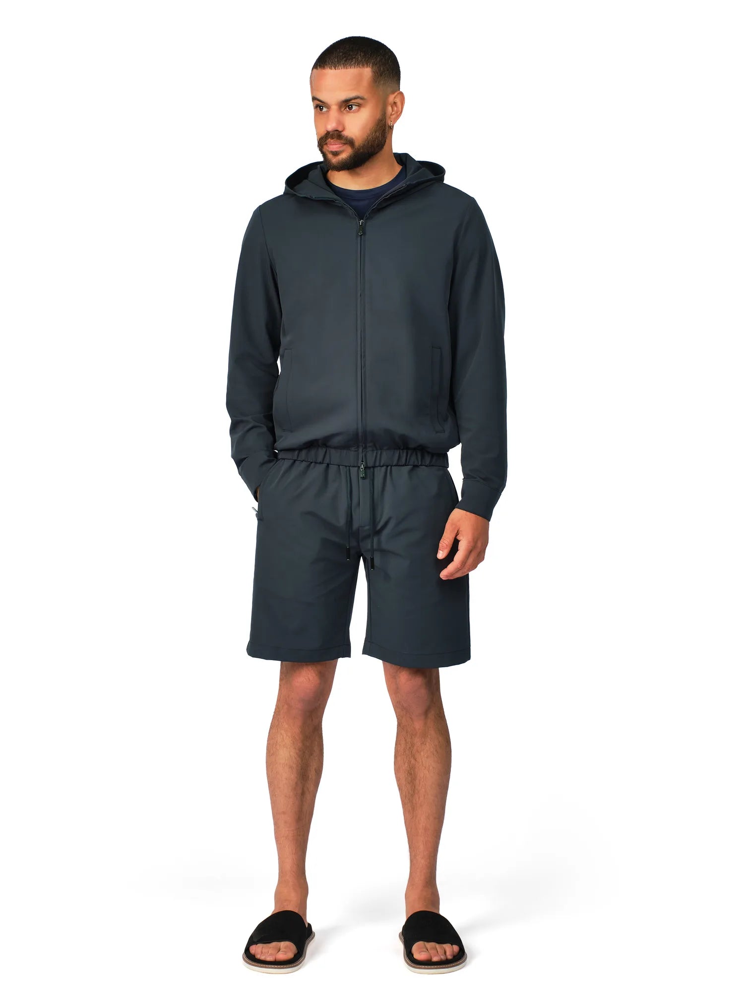 Man wearing a dark gray hoodie and shorts set on a white background