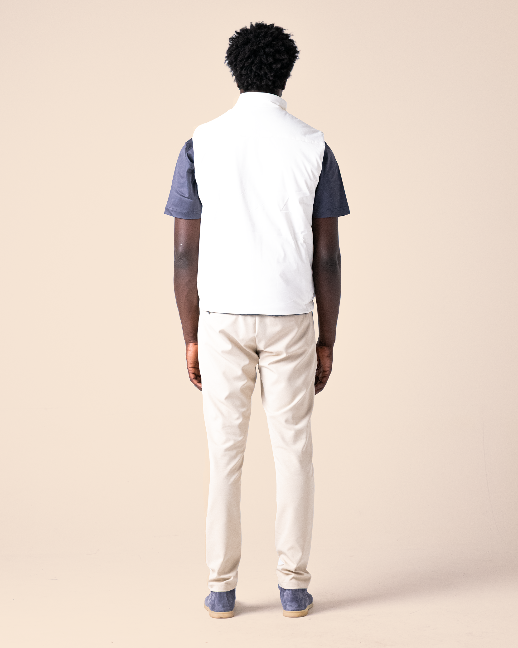 Person wearing a white shirt with navy sleeves and beige pants on a beige background
