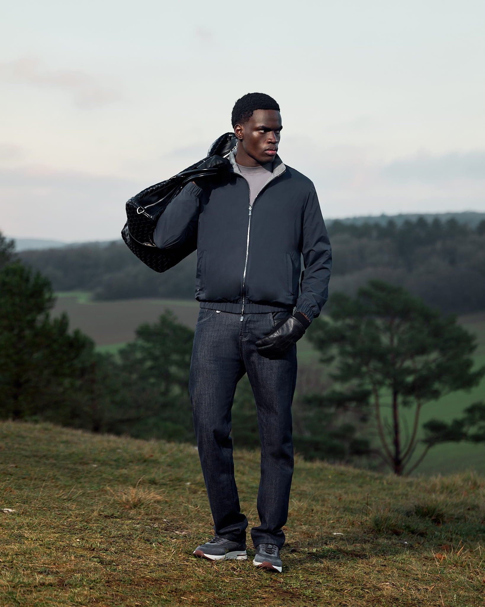 Man holding a black bag outdoors with greenery in the background