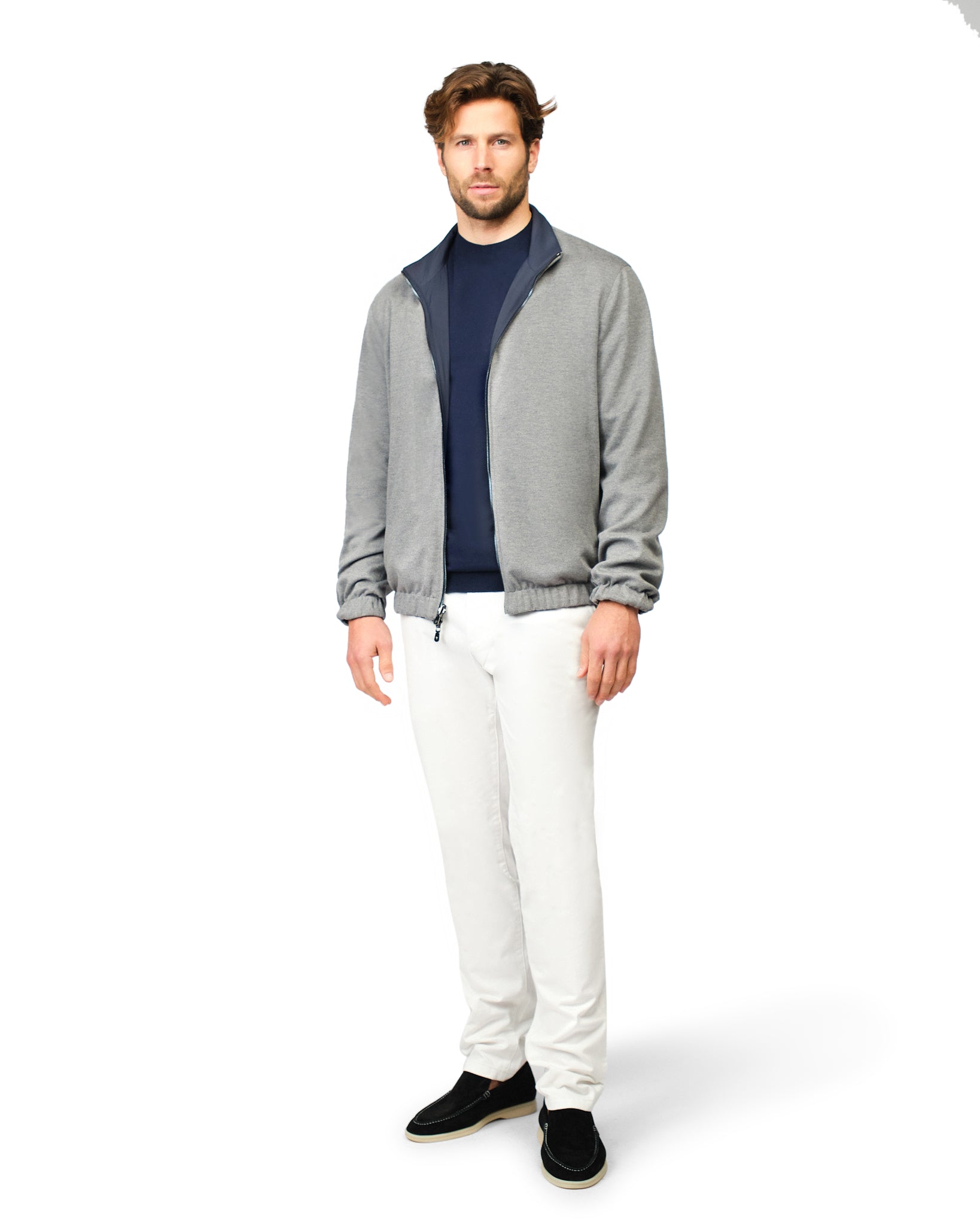 Man wearing a gray jacket, navy shirt, and white pants on a white background