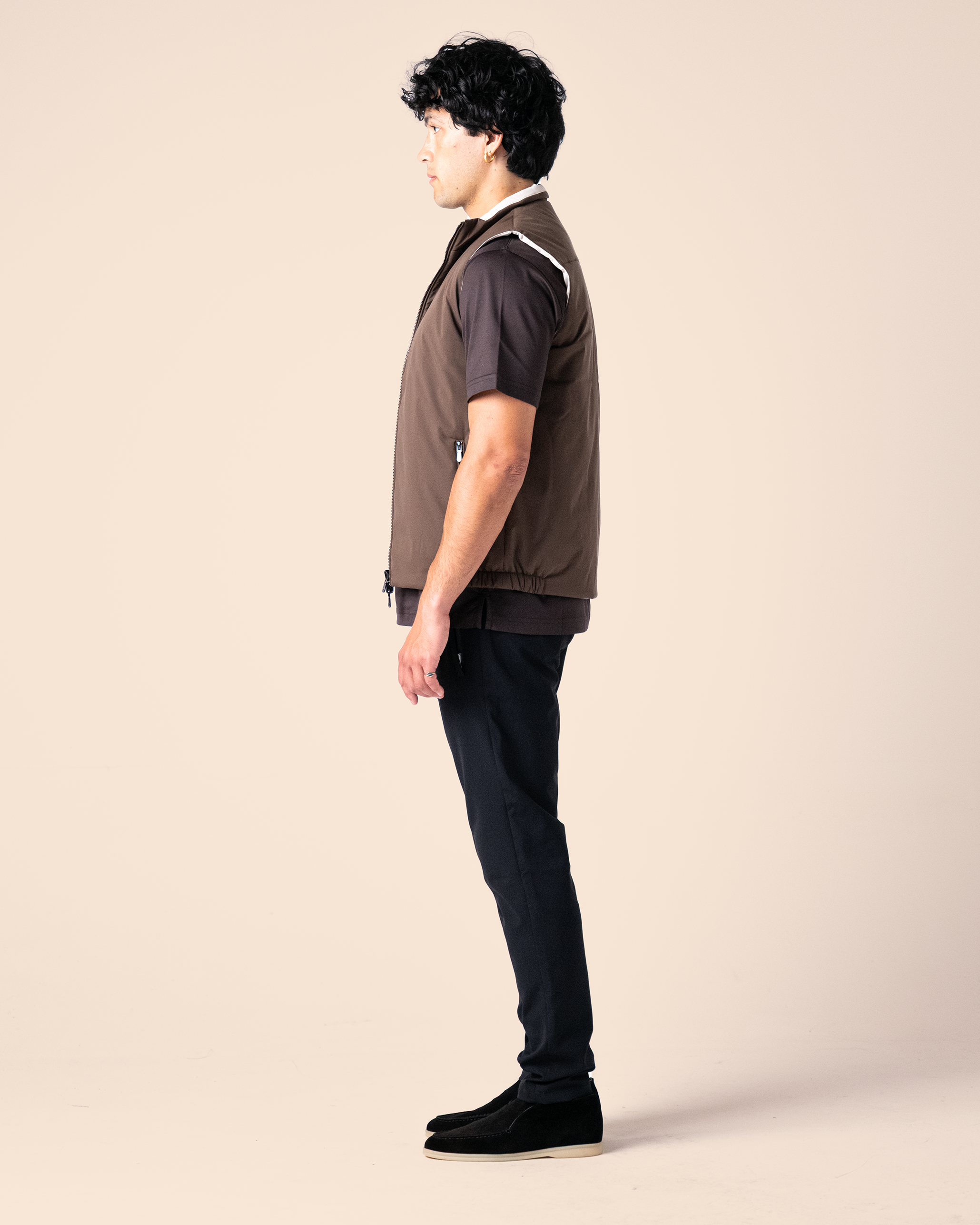 Person wearing a brown shirt and black pants on a beige background