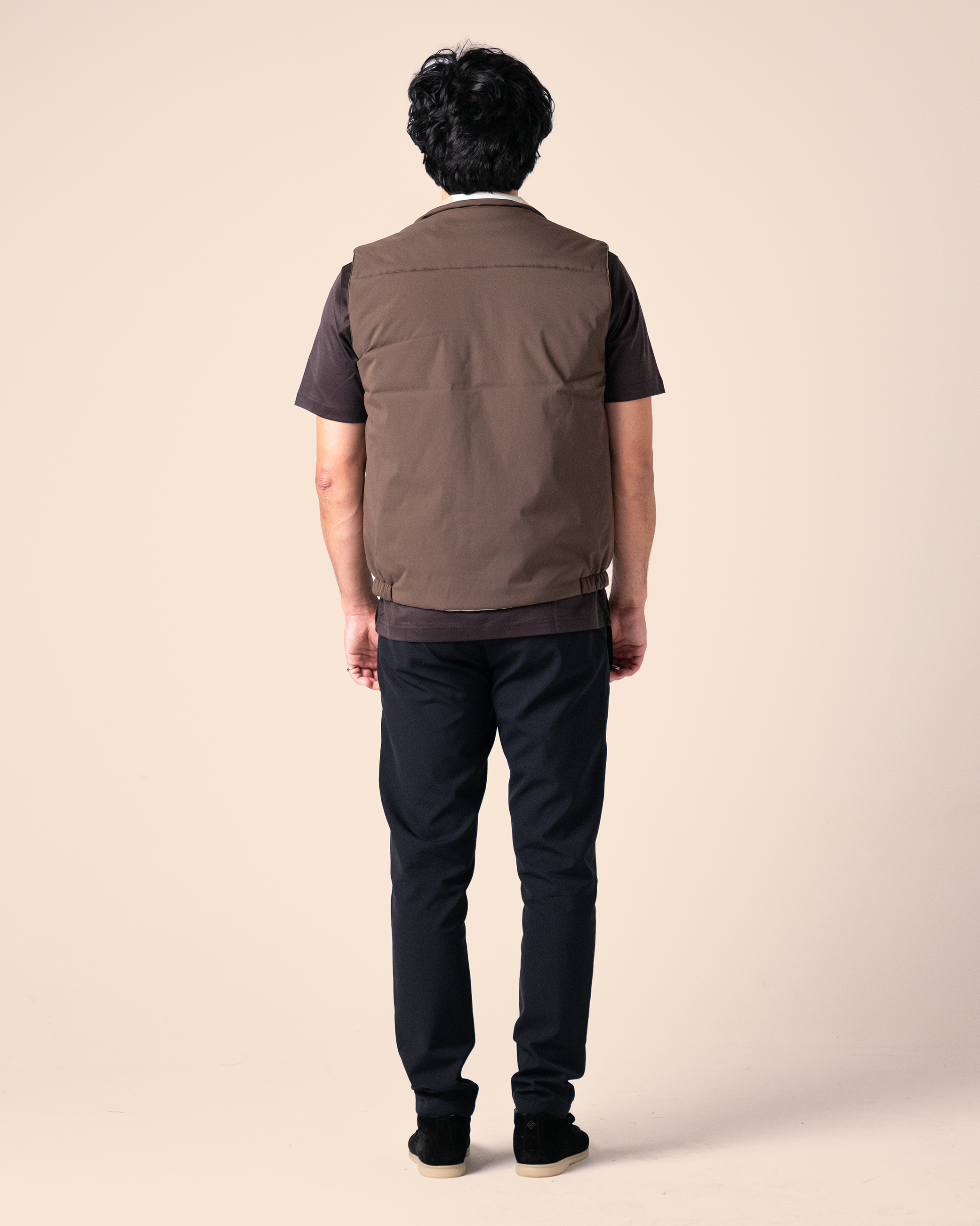 Person wearing a brown vest over a black shirt and pants on a beige background