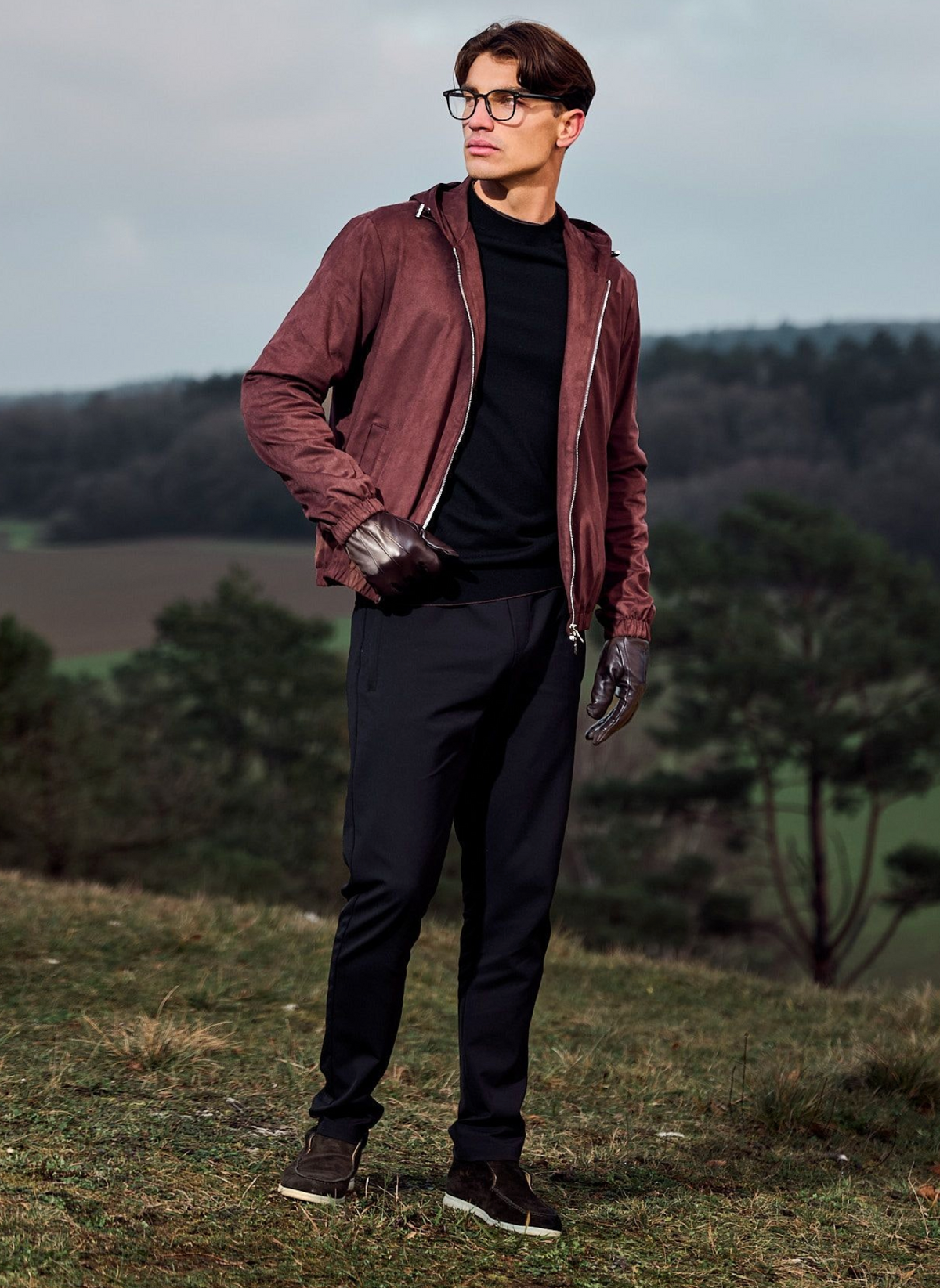 Man wearing a maroon jacket and black pants standing outdoors with trees in the background