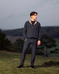 Man wearing a dark gray tracksuit standing outdoors with a landscape background
