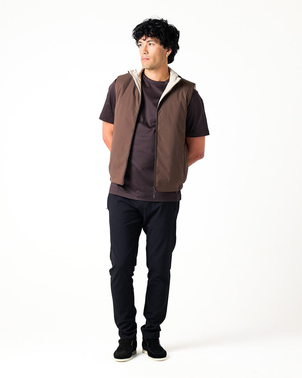 Man wearing a brown vest over a dark shirt with black pants on a white background