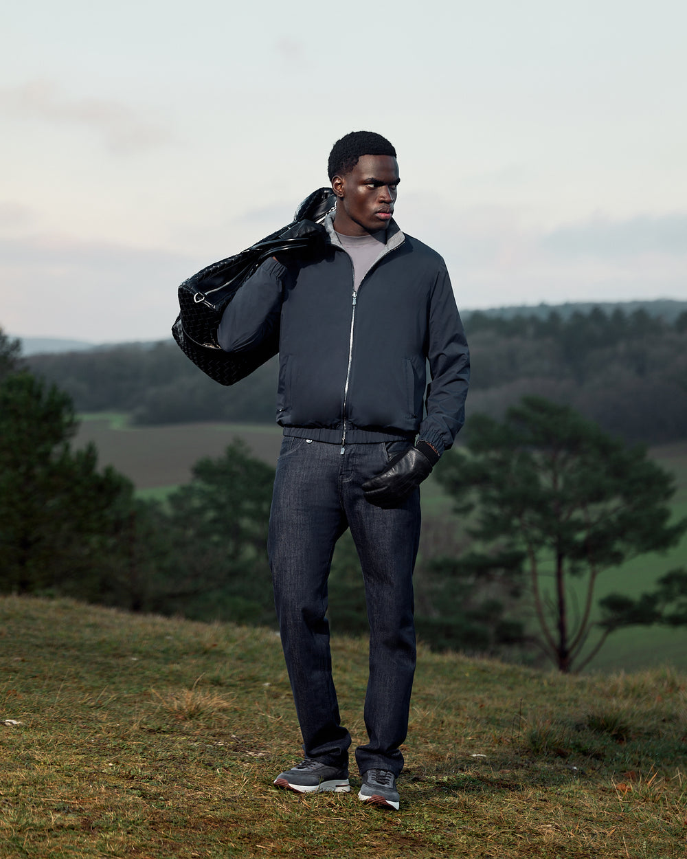 Man holding a black bag outdoors with greenery in the background