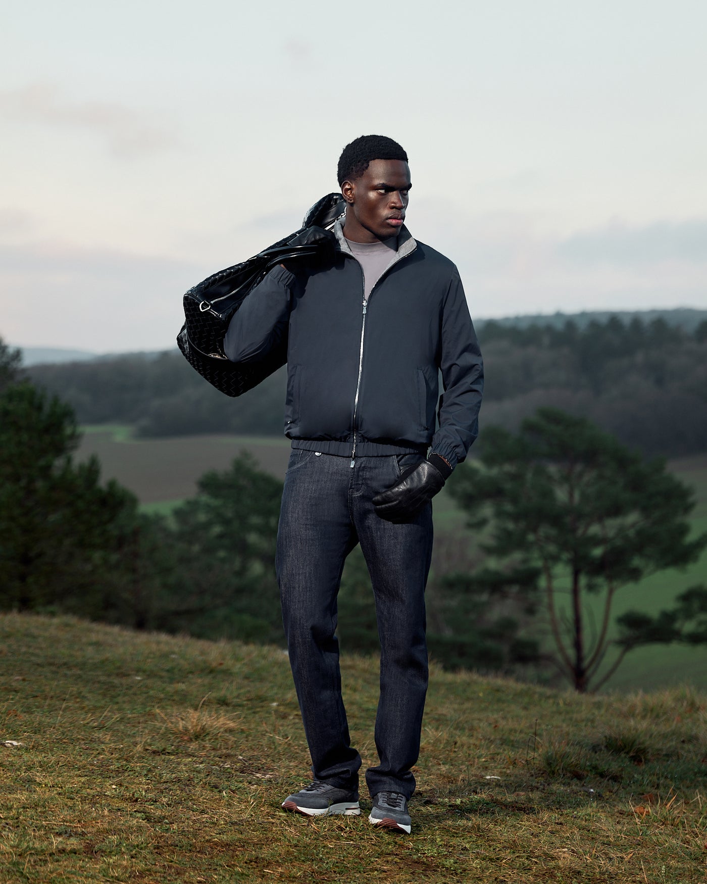 Man holding a black bag outdoors with greenery in the background