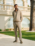 Man in a beige tracksuit standing in front of a large, elegant building with arched windows.