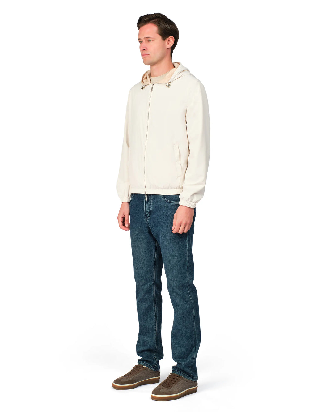 Man wearing a cream jacket, blue jeans, and brown shoes on a white background