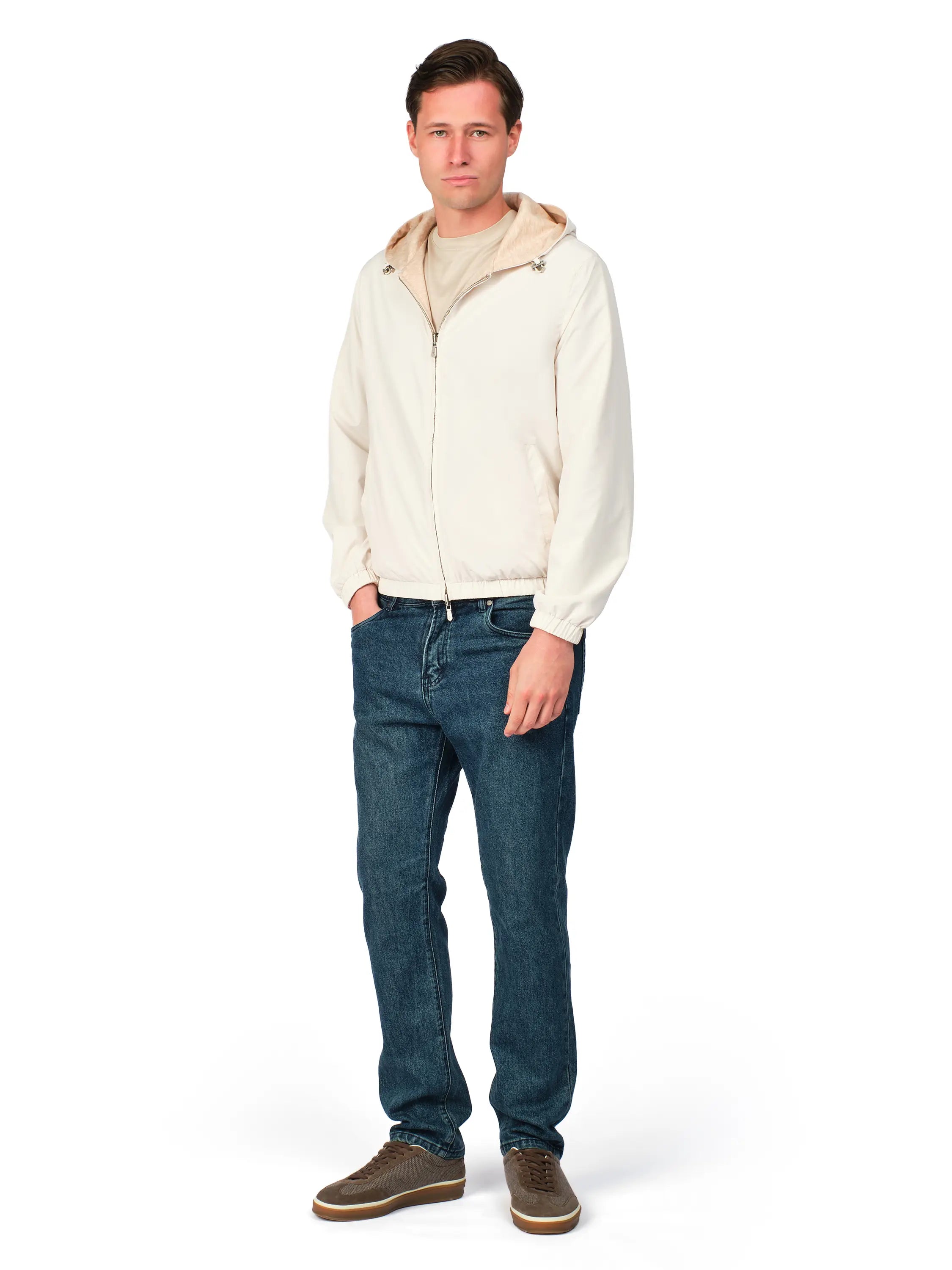 Man wearing a cream jacket, blue jeans, and brown shoes on a white background