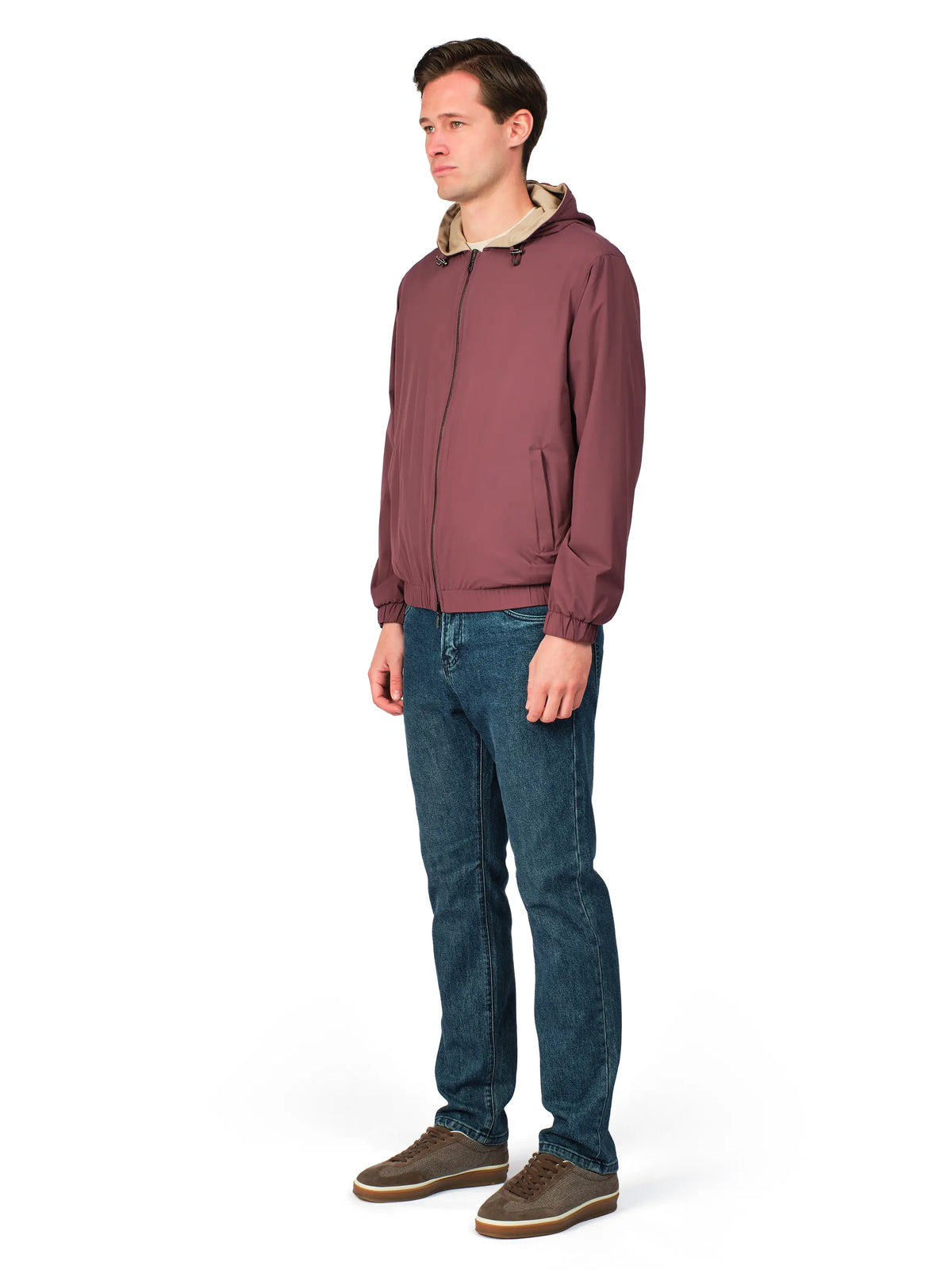Man wearing a maroon jacket and blue jeans on a white background