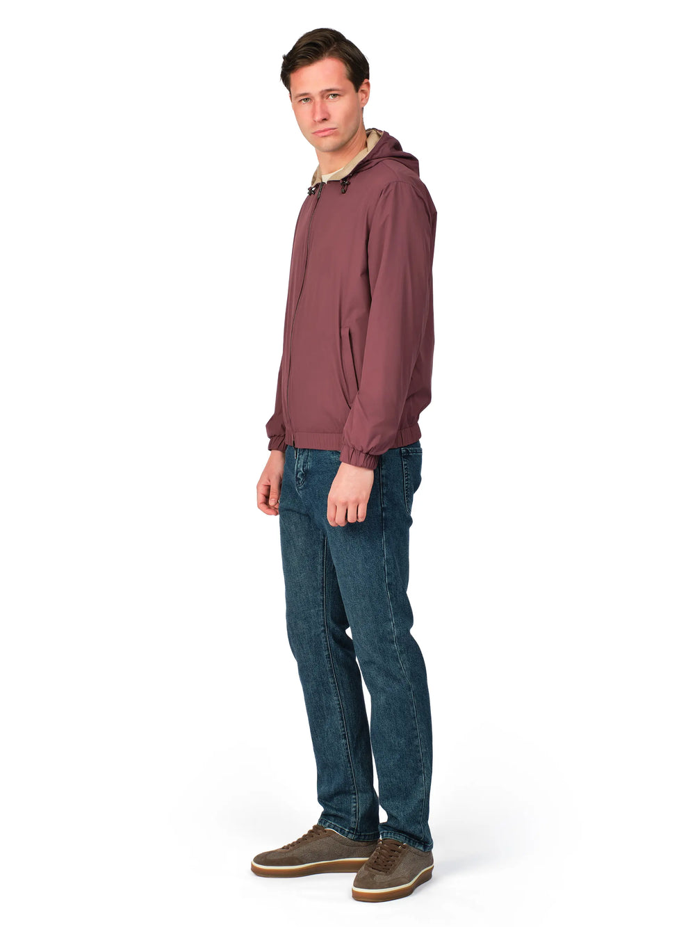 Man wearing a maroon jacket and blue jeans on a white background