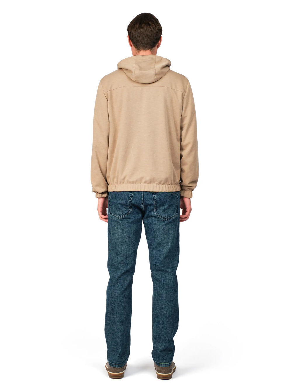 Person wearing a beige jacket and blue jeans on a white background