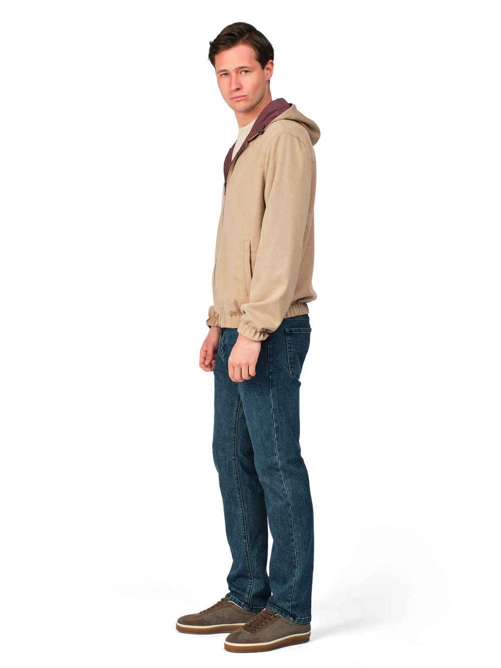 Man wearing a beige hoodie with a maroon hood and blue jeans on a white background