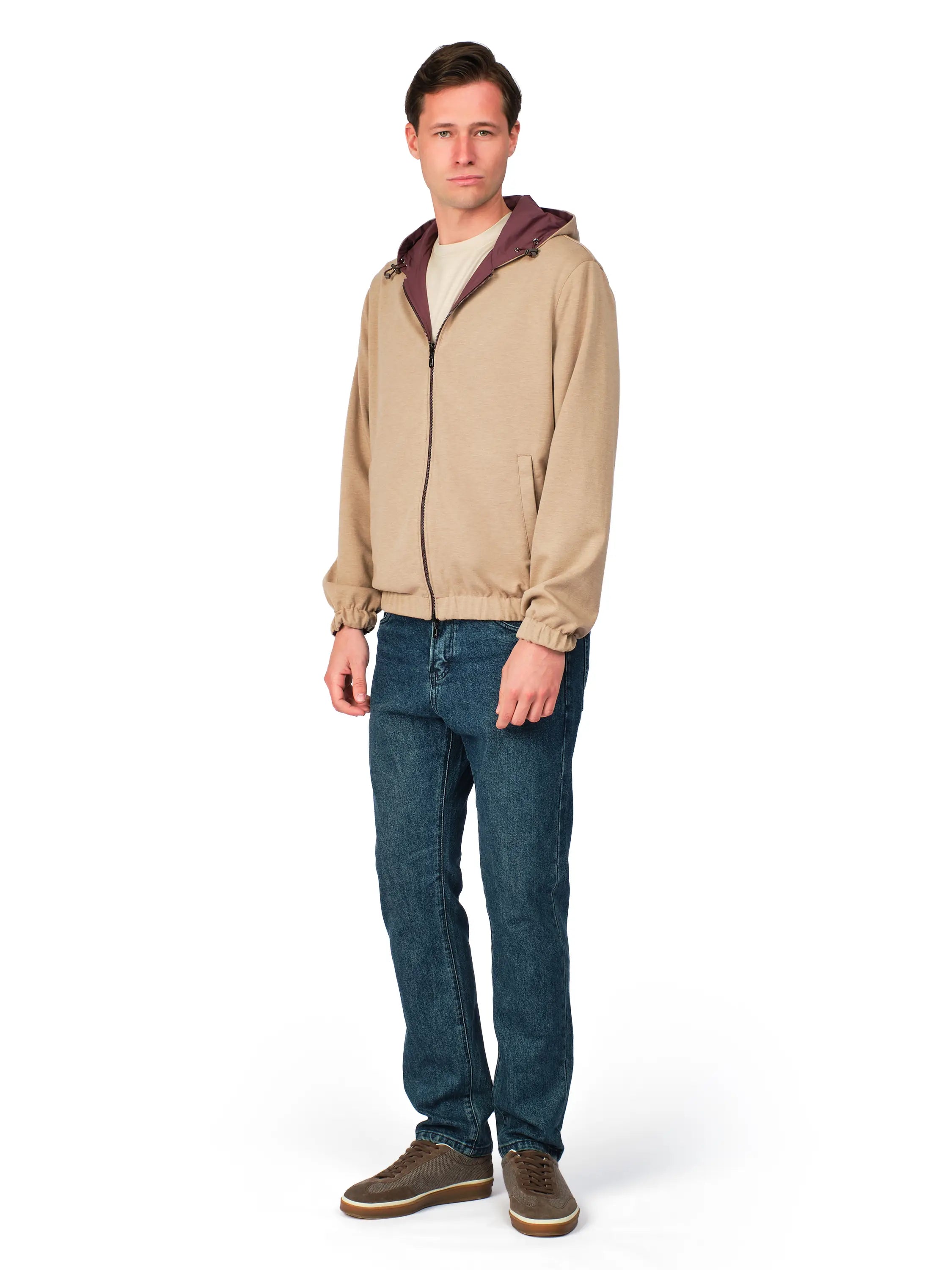 Man wearing a beige jacket with a maroon hood and blue jeans on a white background