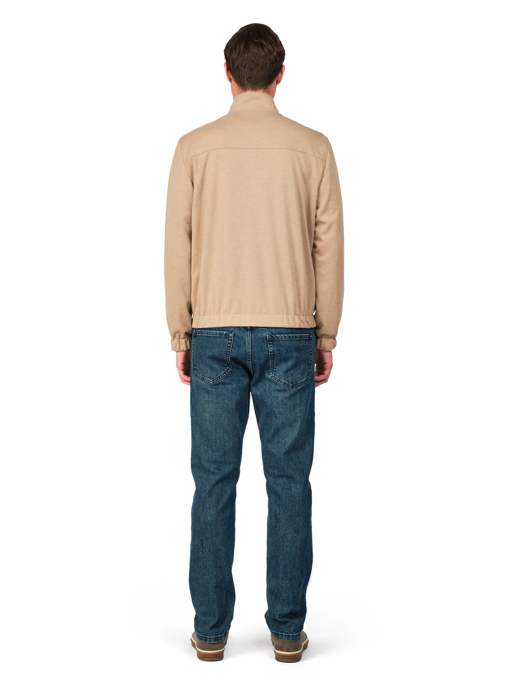 Man wearing a beige sweater and blue jeans on a white background