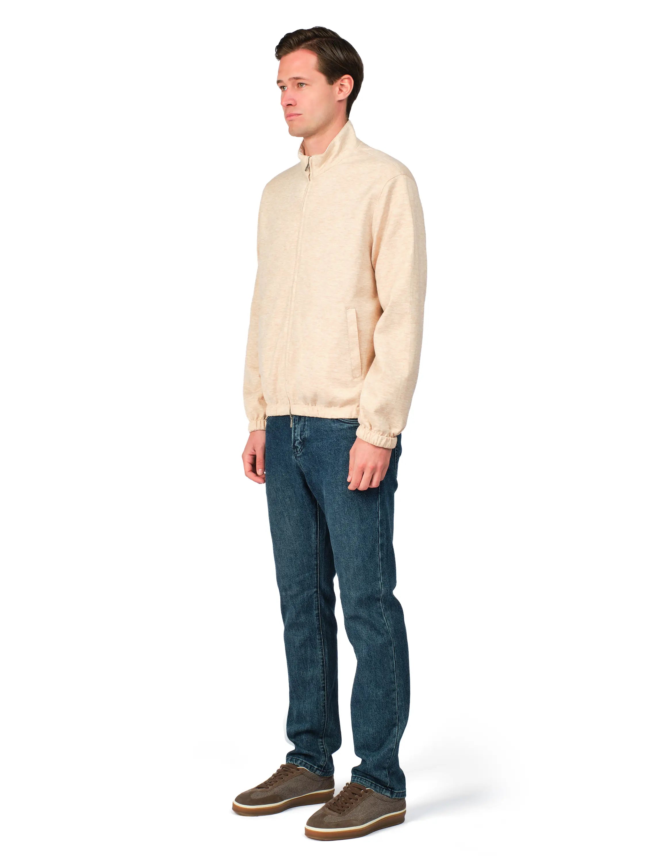 Man wearing a beige sweater and blue jeans on a white background