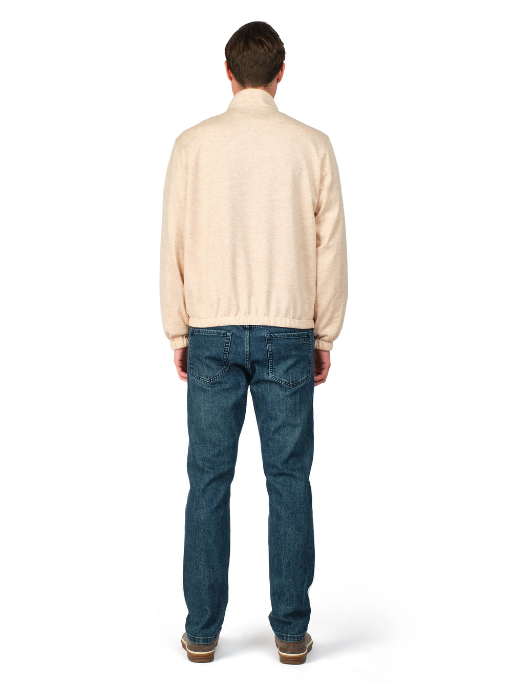 Man wearing a beige sweater and blue jeans on a white background