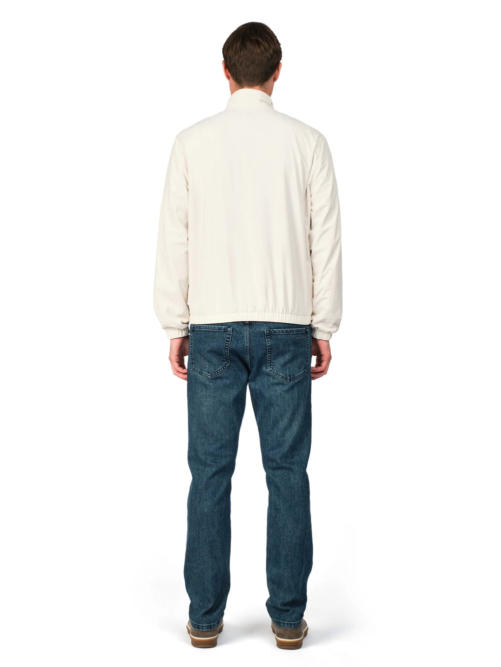 Man wearing a cream shirt and blue jeans on a white background