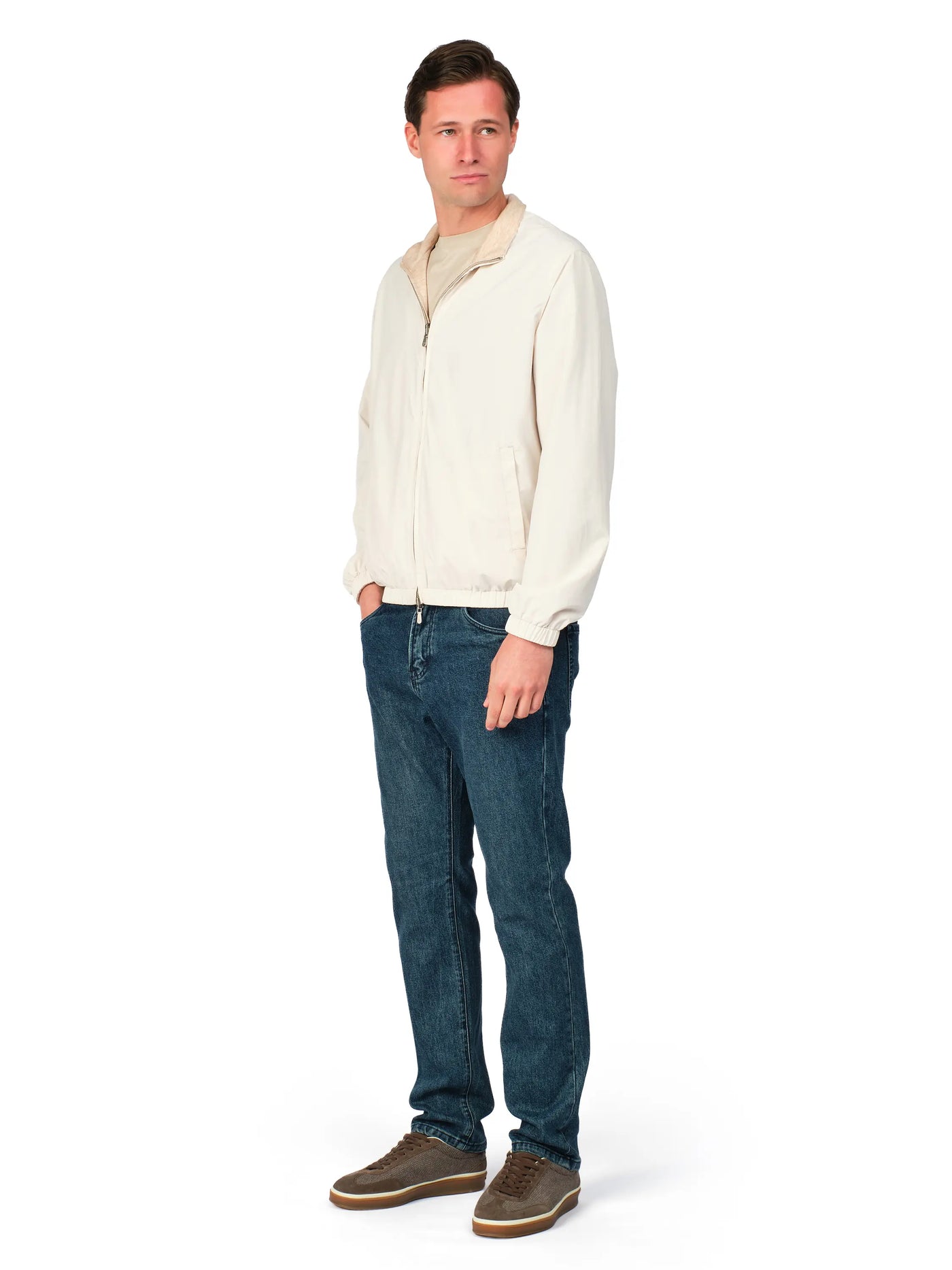 Man wearing a cream jacket and blue jeans on a white background
