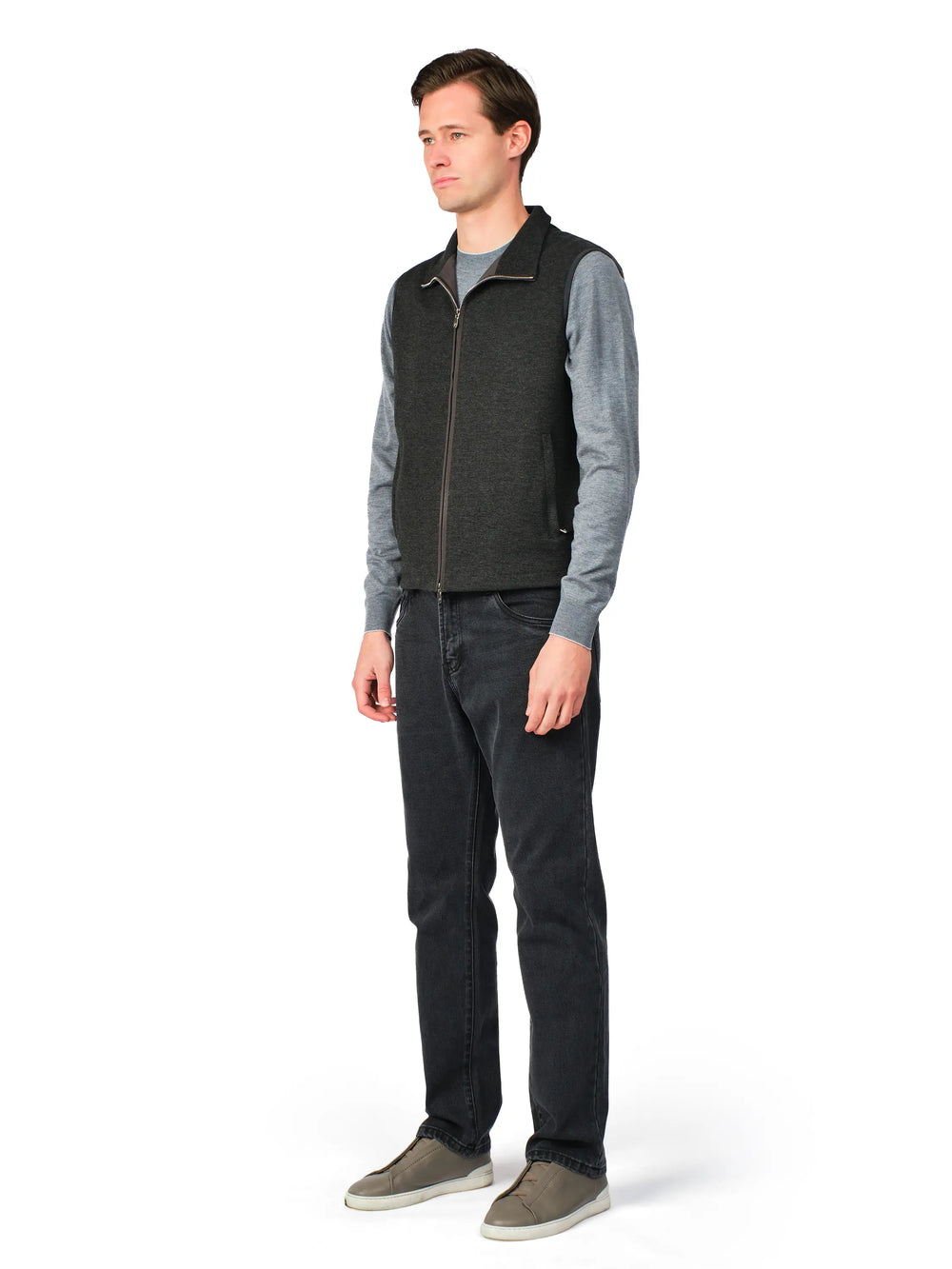 Man wearing a gray vest over a long-sleeve shirt with dark pants on a white background