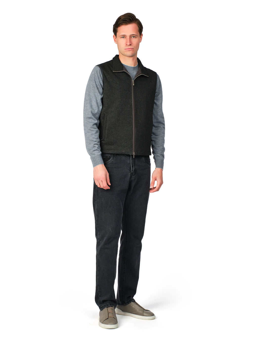 Man wearing a gray sweater, black vest, and dark jeans on a white background