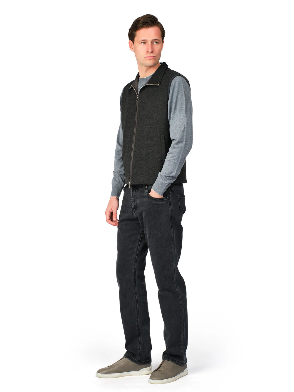 Man wearing a gray sweater, black vest, and dark jeans on a white background
