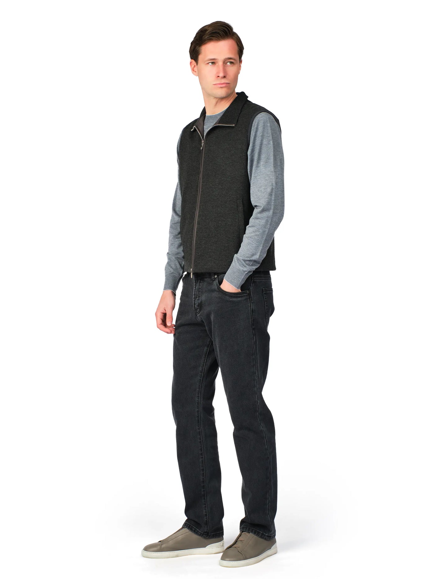 Man wearing a gray sweater, black vest, and dark jeans on a white background