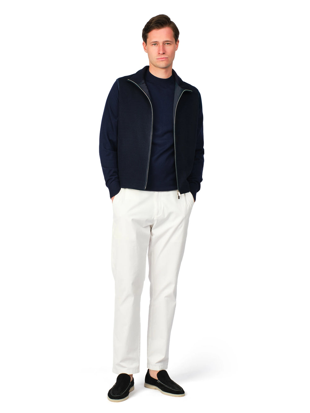 Man wearing a navy jacket, black shirt, white pants, and black shoes on a white background