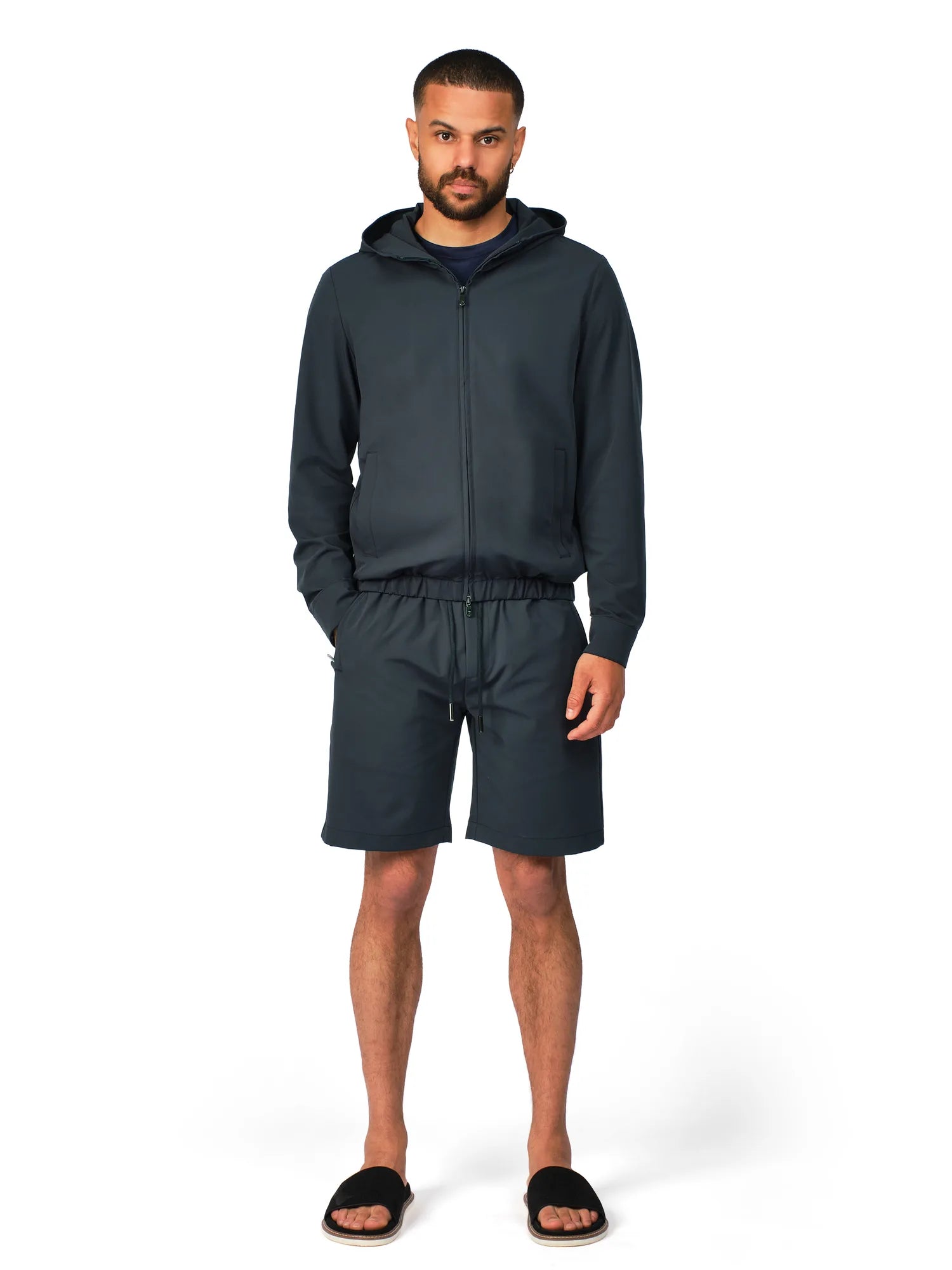 Man wearing a dark gray hoodie and shorts set on a white background