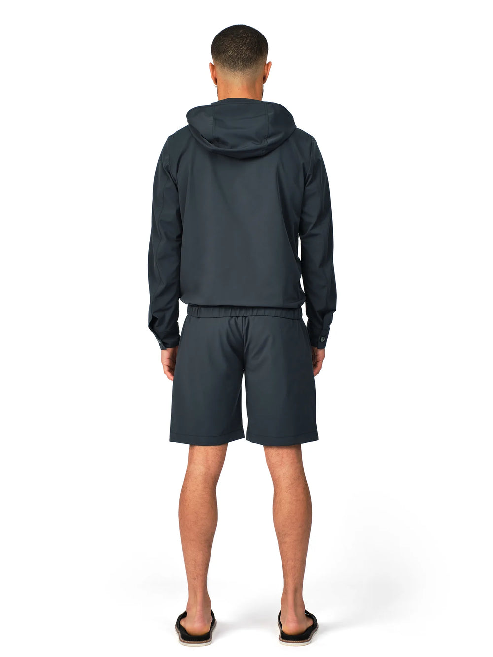 Person wearing a dark gray hoodie and shorts set on a white background