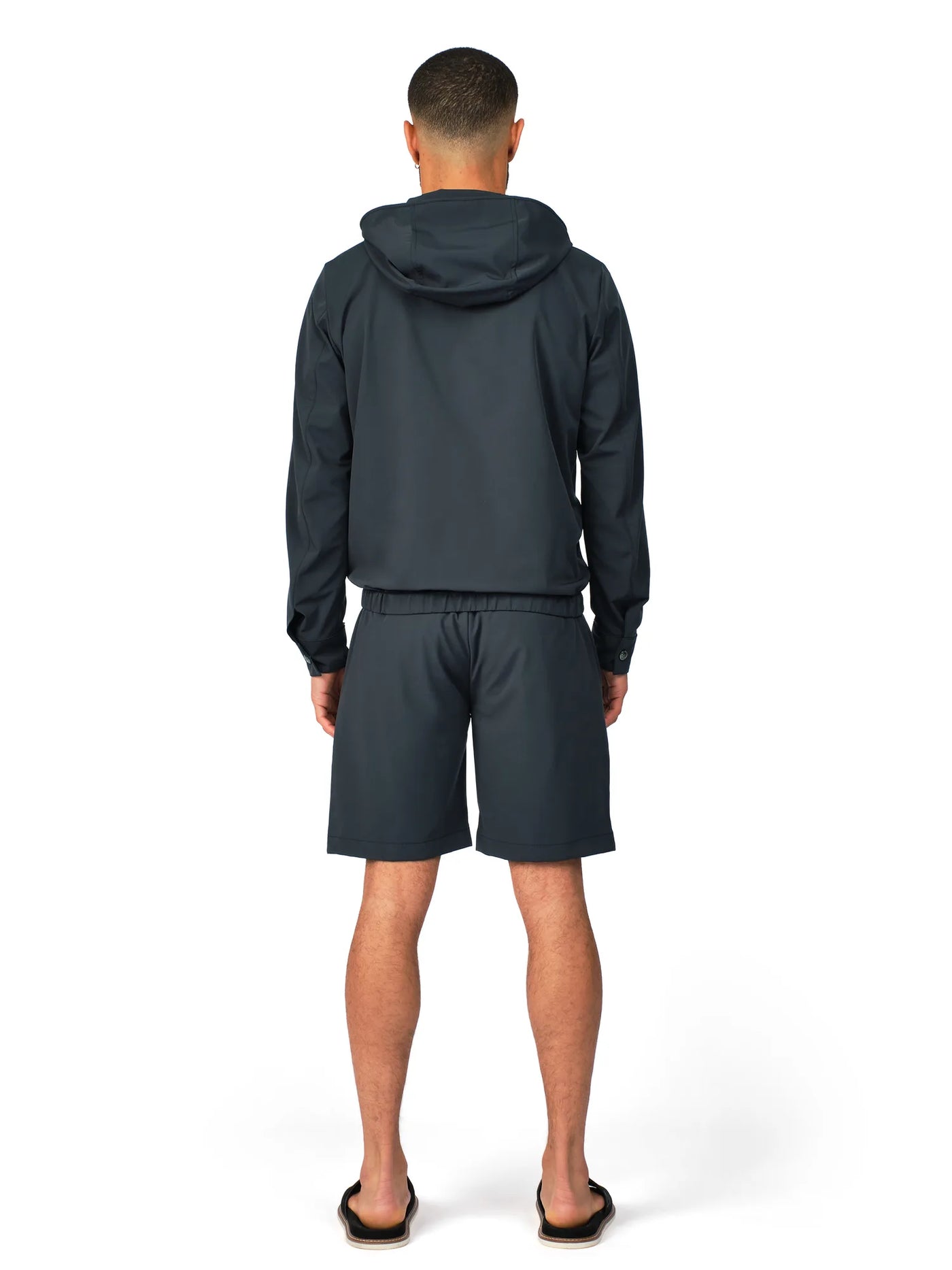 Person wearing a dark gray hoodie and shorts set on a white background