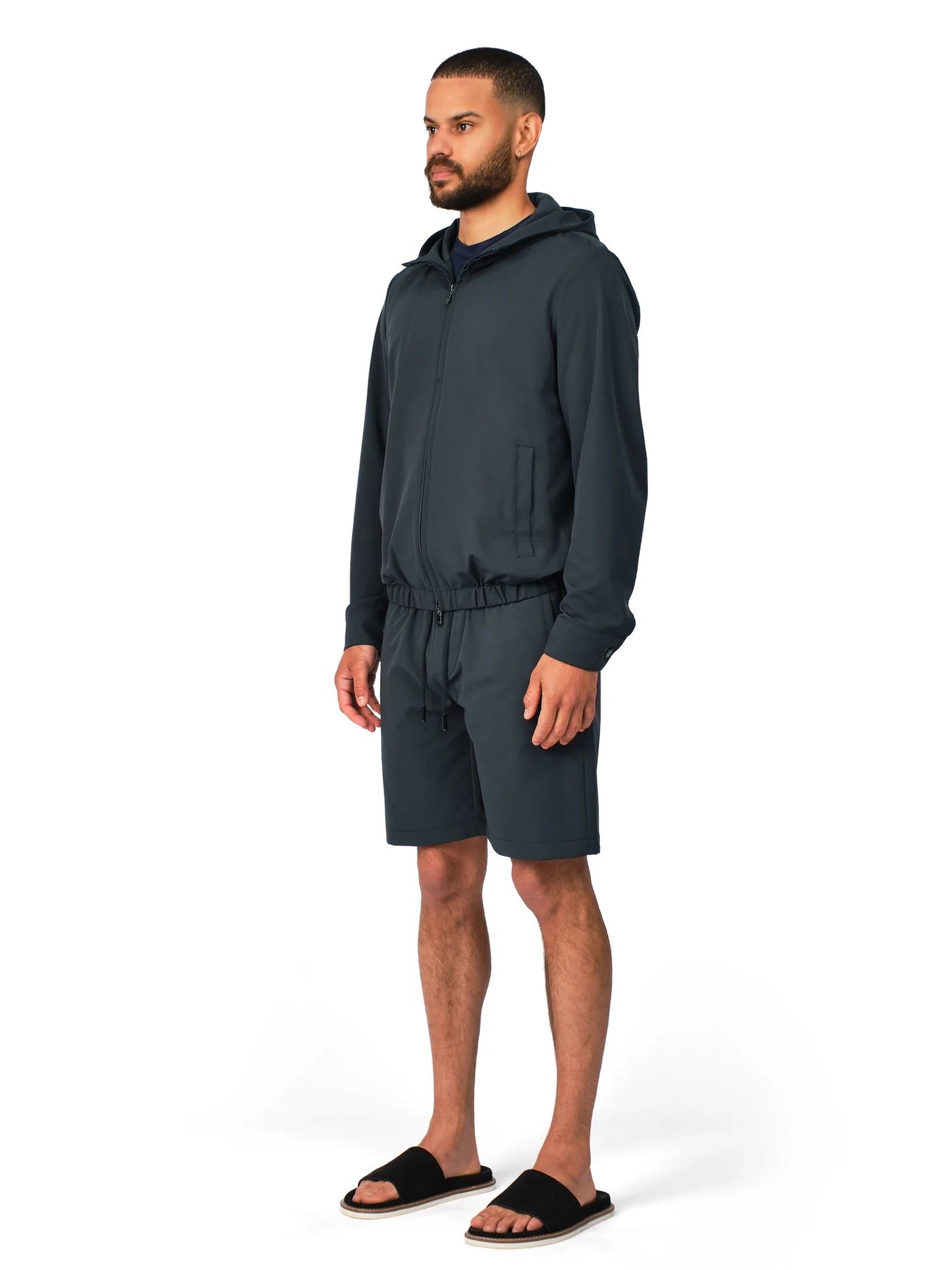 Man wearing a dark gray hoodie and shorts set on a white background