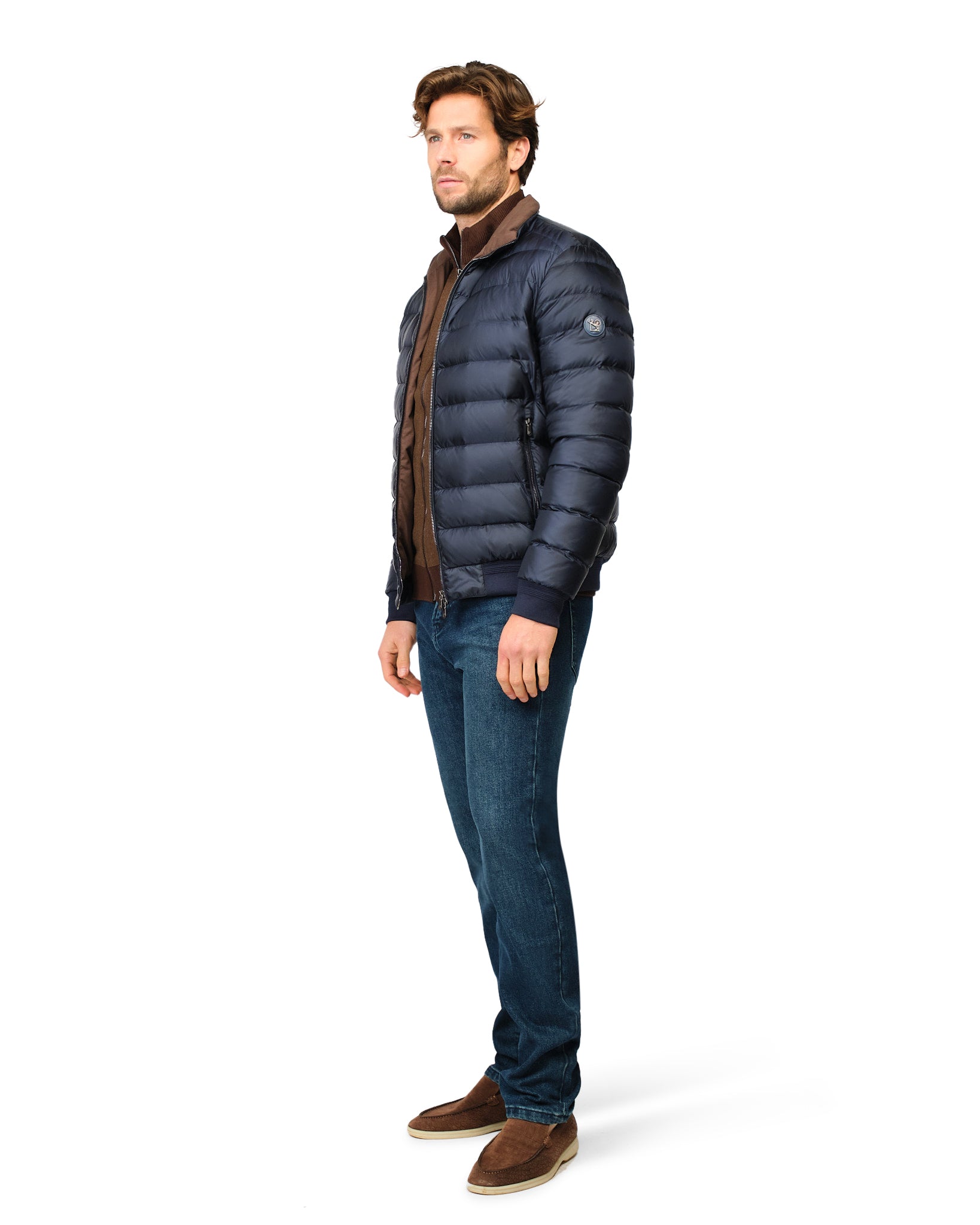 Man wearing a navy puffer jacket, brown scarf, and jeans on a white background