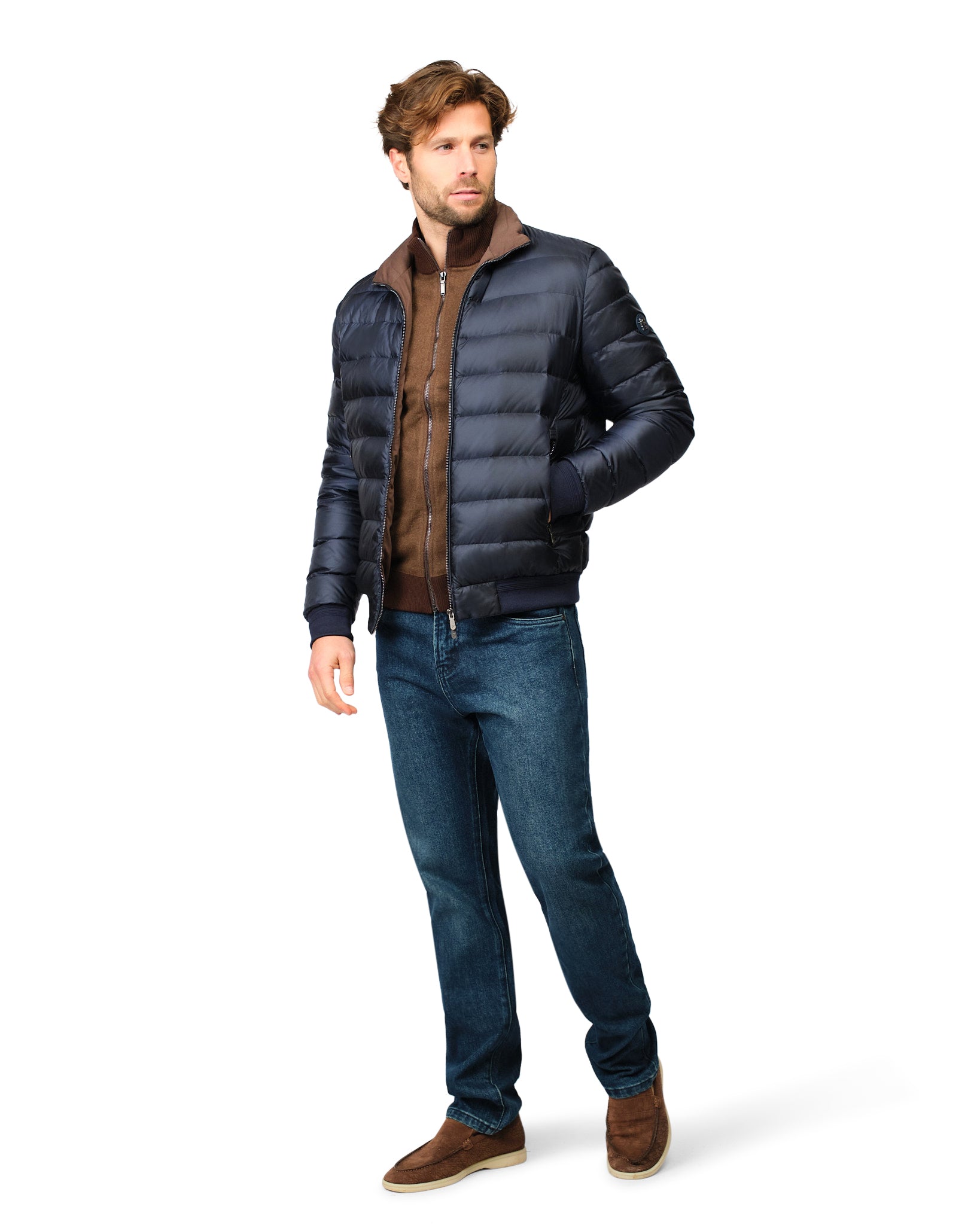 Man wearing a black puffer jacket, brown shirt, blue jeans, and brown shoes on a white background