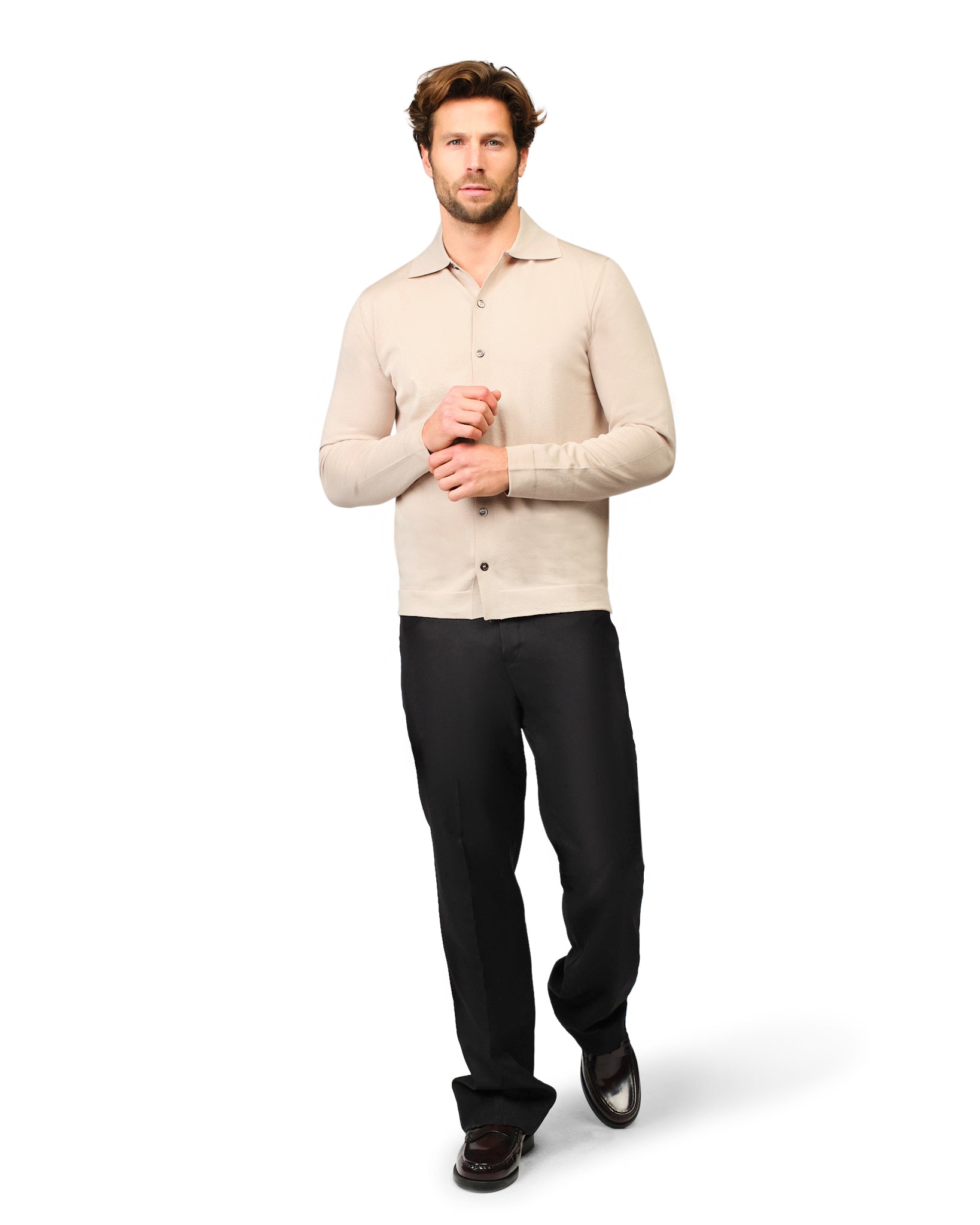 Man wearing a beige sweater and black pants on a white background