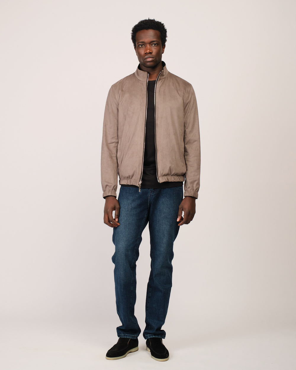 Man wearing a beige jacket and blue jeans on a white background