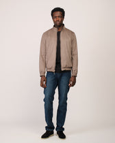 Man wearing a beige jacket and blue jeans on a white background