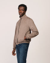 Man wearing a beige jacket and blue jeans on a plain background