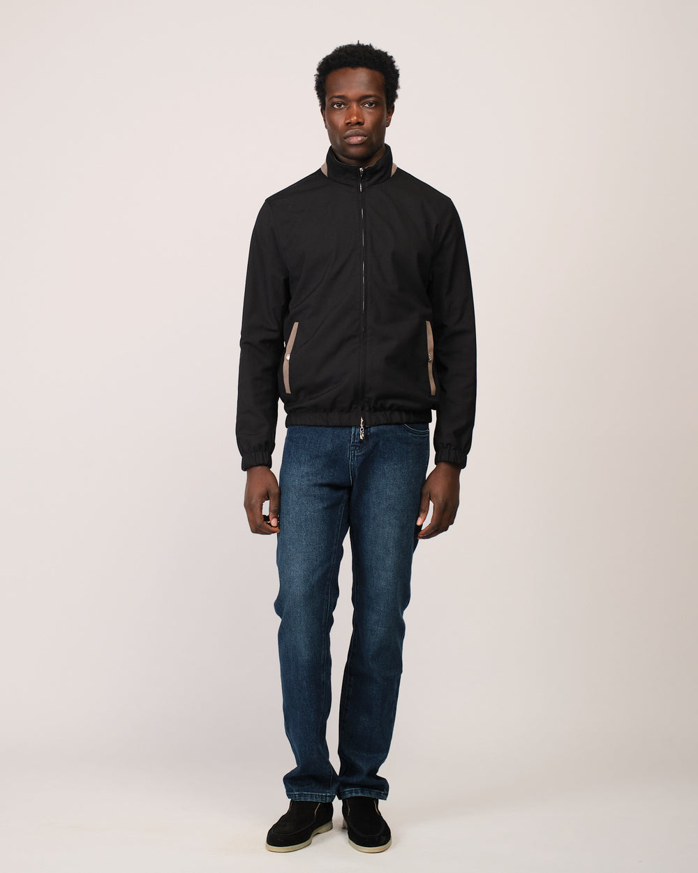 Man wearing a black jacket and blue jeans on a white background