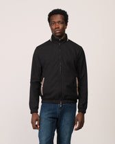 Man wearing a black jacket and blue jeans on a plain background