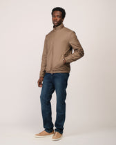 Man wearing a beige jacket and blue jeans on a white background