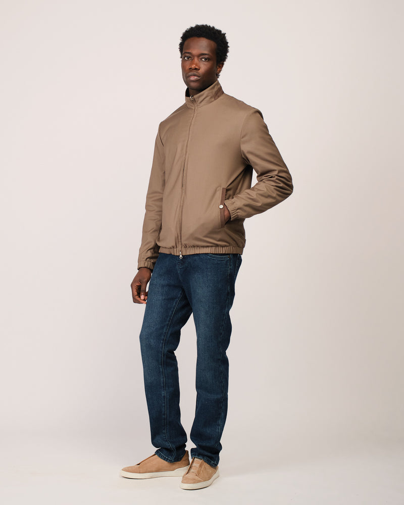 Man wearing a beige jacket and blue jeans on a white background