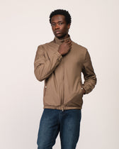 Man wearing a brown jacket and blue jeans on a plain background